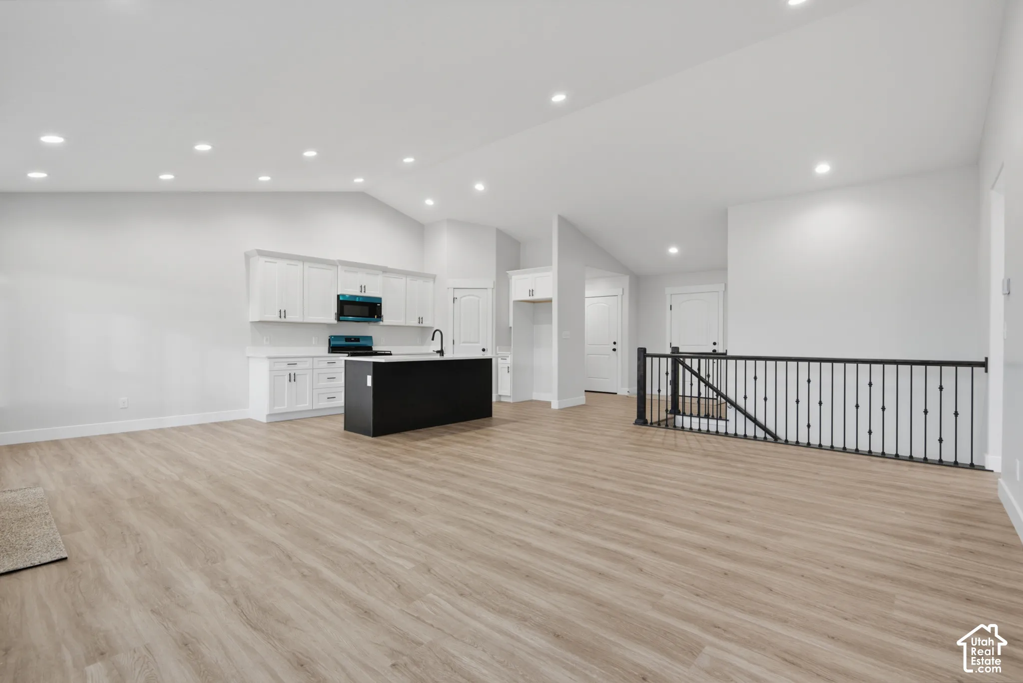 Open-concept interior featuring vaulted ceilings, recessed lighting, wood-finish flooring, a kitchen island with a dark base, and iron staircase railing