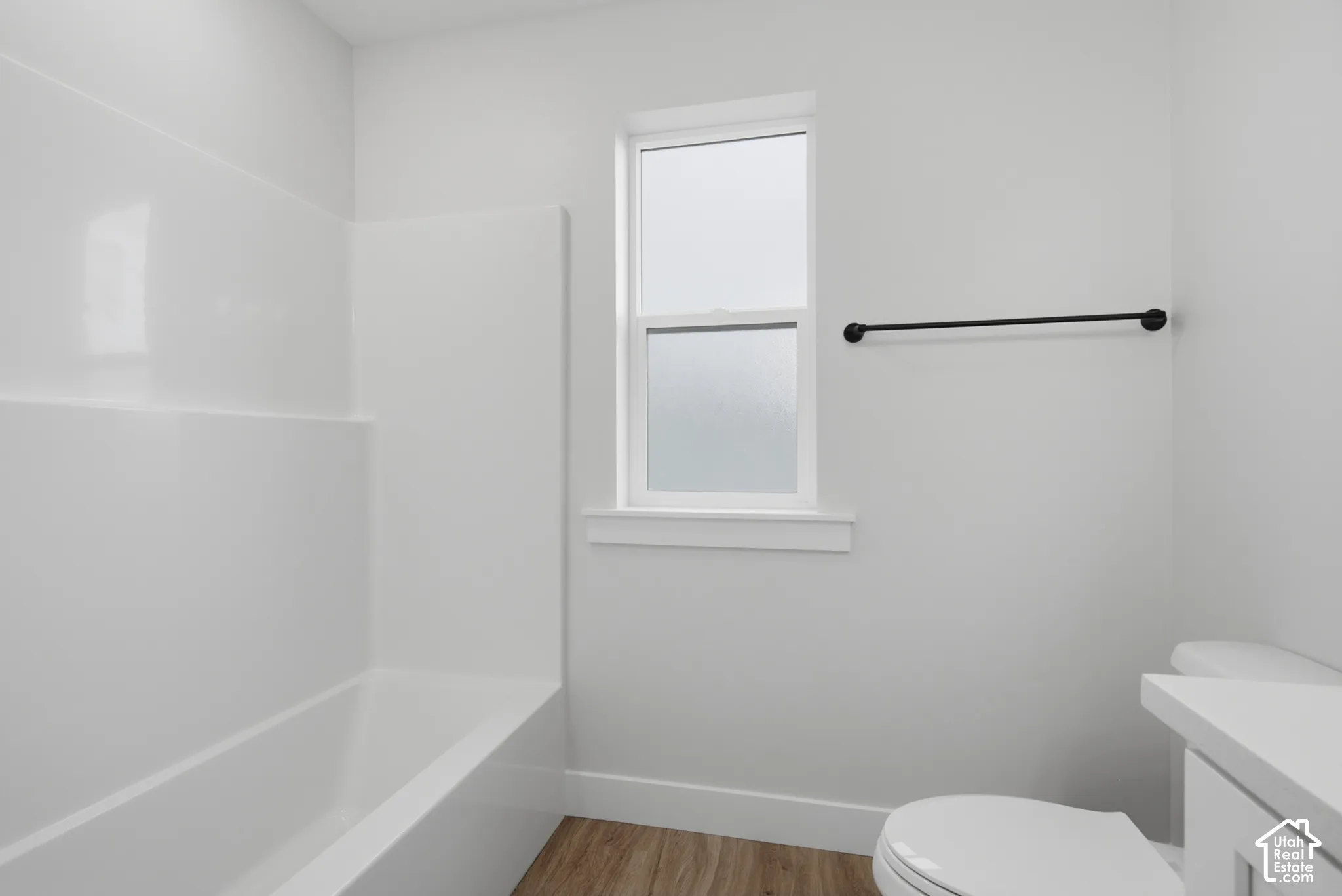Full-height white tub surround, frosted glass window, matte black towel bar, and wood-finish flooring