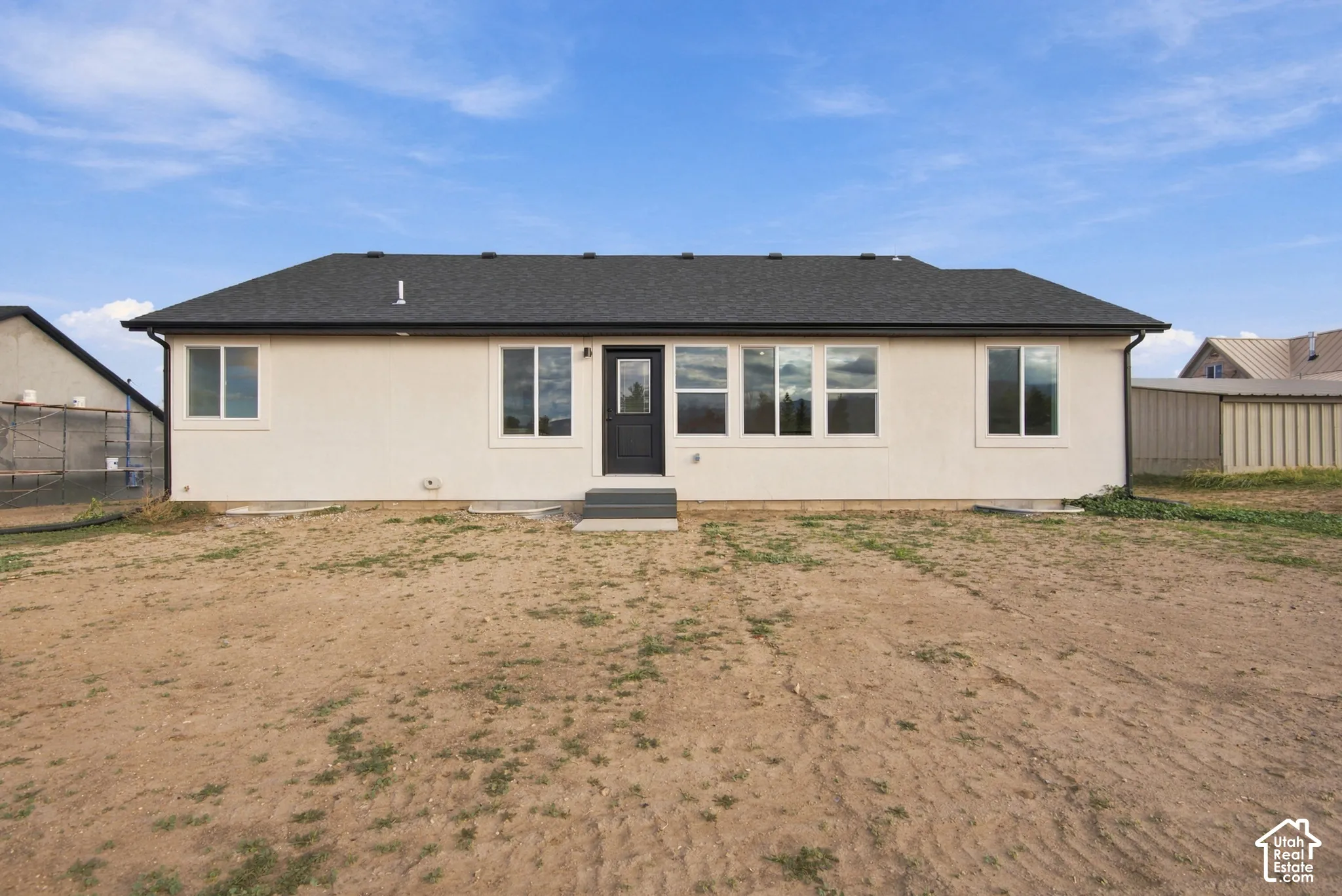 Single-story residence featuring a light-colored stucco exterior, dark asphalt shingle roof, dark-framed windows, and a black exterior entry door