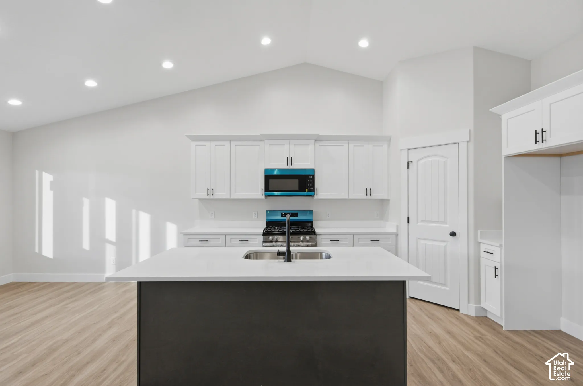 Kitchen featuring a center island with a stone countertop, white cabinetry, wood-finish flooring, vaulted ceilings, and recessed lighting