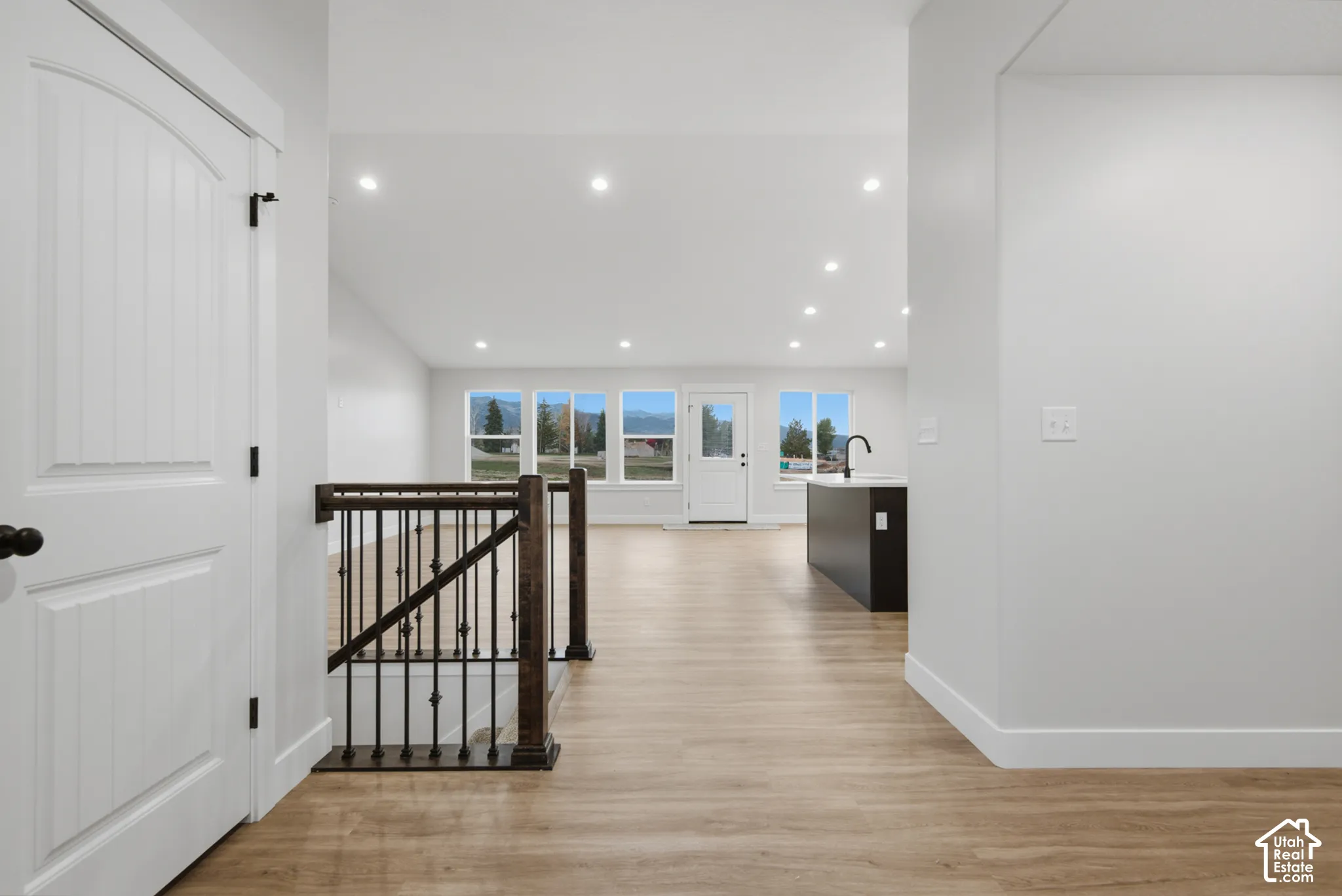 Open-concept interior featuring vaulted ceilings, recessed lighting, wood-finish flooring, and a metal-spindle staircase railing