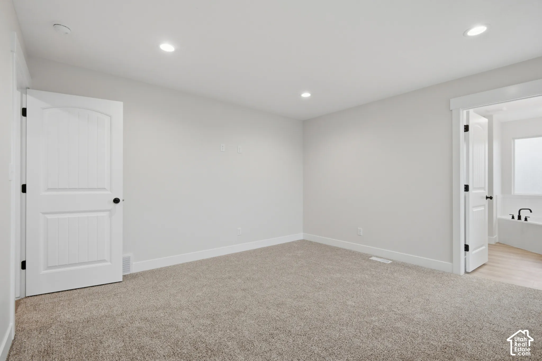 Neutral-toned interior space featuring wall-to-wall carpeting, recessed ceiling lighting, and two-panel interior doors with matte black hardware