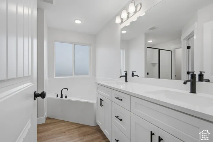 Dual vanity featuring white cabinetry, solid-surface countertops, and matte black hardware, paired with a soaking tub and wood-finish flooring