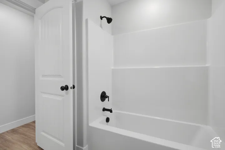 Full-height tub and shower surround with matte black plumbing fixtures, arched two-panel interior door, and wood-finish flooring