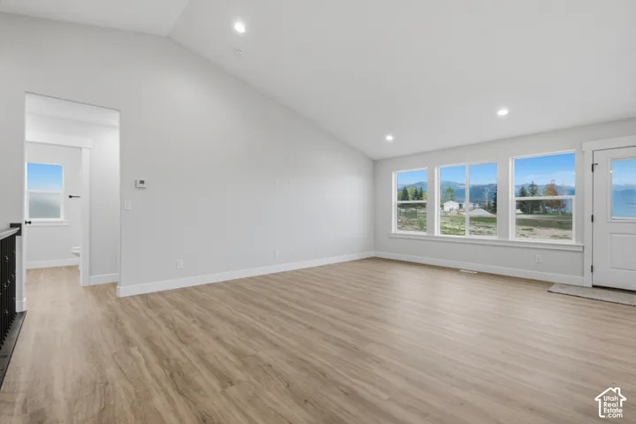 Vaulted ceilings, wood-finish flooring, recessed lighting, and expansive windows featuring a mountain backdrop