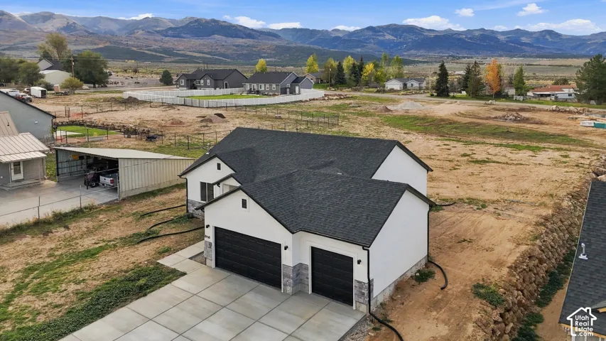 Single-story residence featuring a multi-gabled asphalt shingle roof, two-car garage with black paneled doors, stone veneer accents, and an expansive mountain backdrop