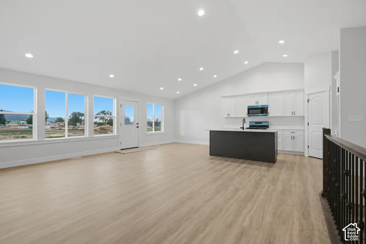 Vaulted ceilings featuring recessed lighting, wood-finish flooring, kitchen island with a contrasting base, white cabinetry, and large windows