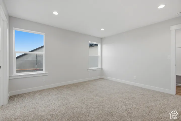 Neutral-toned walls, recessed ceiling lighting, plush wall-to-wall carpeting, and dual windows with crisp white casing
