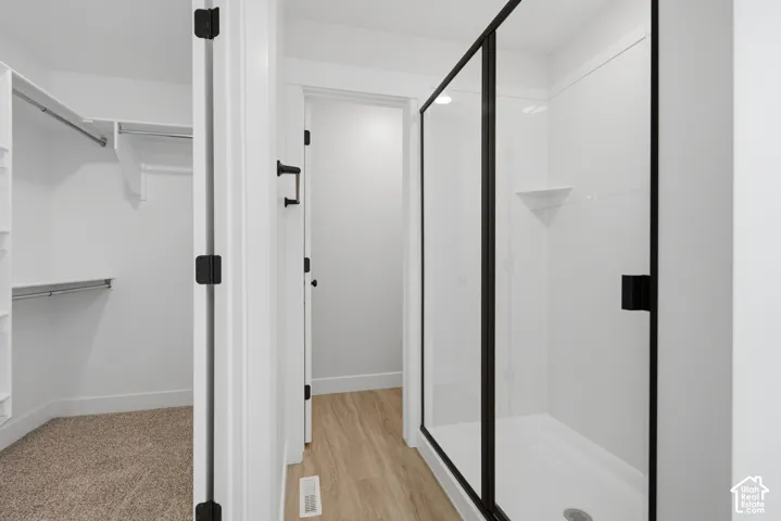 Walk-in closet with built-in shelving, shower enclosure featuring matte black framing and hardware, and wood-finish flooring