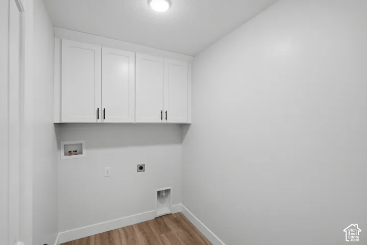 Utility room featuring white shaker-style wall cabinets with matte black hardware, recessed washer and dryer hookups, and wood-finish flooring