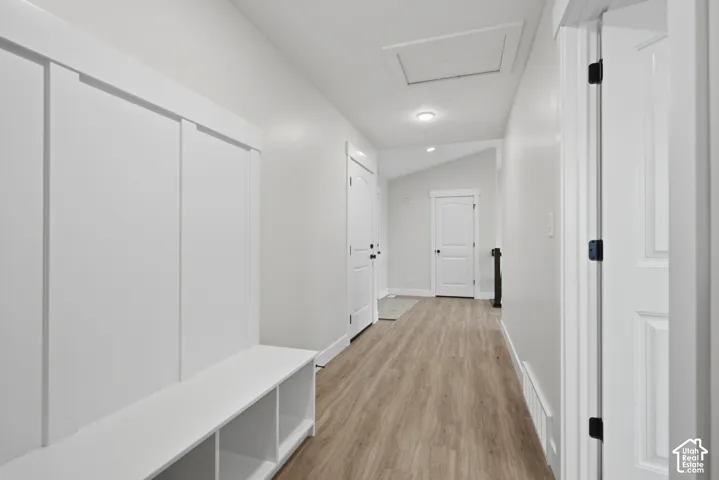 Hallway featuring wood-finish flooring, white board-and-batten wainscoting, built-in cubby storage, arched-top interior doors, and vaulted ceilings