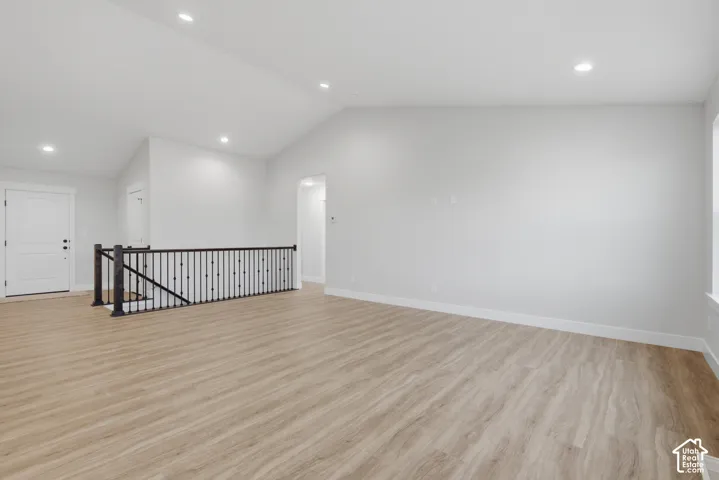 Vaulted ceiling featuring recessed lighting, wood-finish flooring, and a metal-spindle stair railing