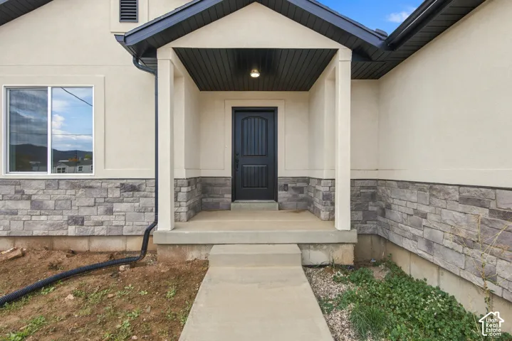 Exterior entry featuring a covered porch, stone veneer facade, stucco siding, and a dark-finished arched panel front door