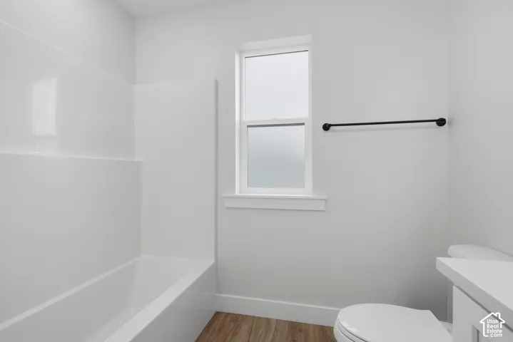 Full-height white tub surround, frosted glass window, matte black towel bar, and wood-finish flooring