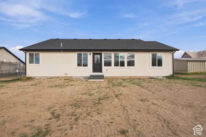 Single-story residence featuring a light-colored stucco exterior, dark asphalt shingle roof, dark-framed windows, and a black exterior entry door