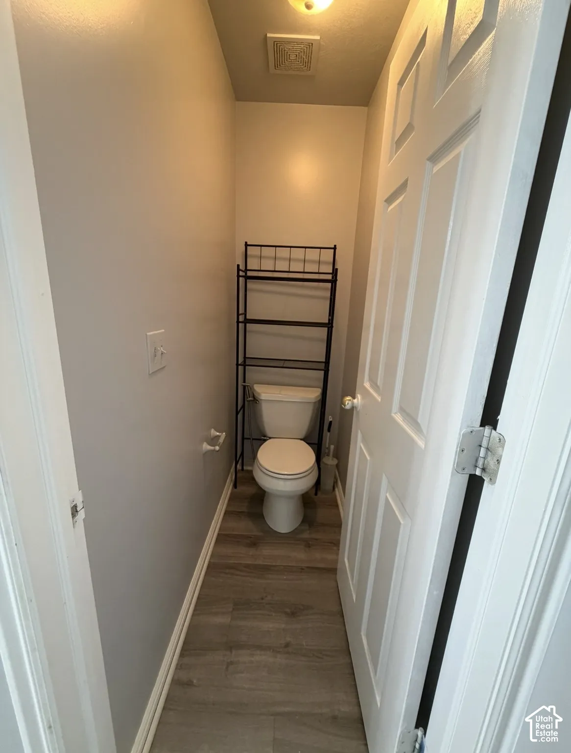 Restroom featuring wood-finish flooring, a two-piece toilet, and a six-panel door