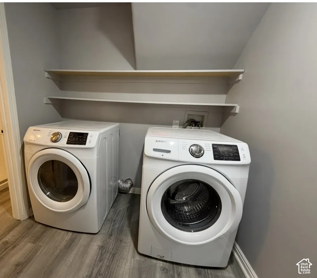 Utility space featuring wood-finish flooring, dual wall-mounted shelving units, and dedicated washer and dryer hookups