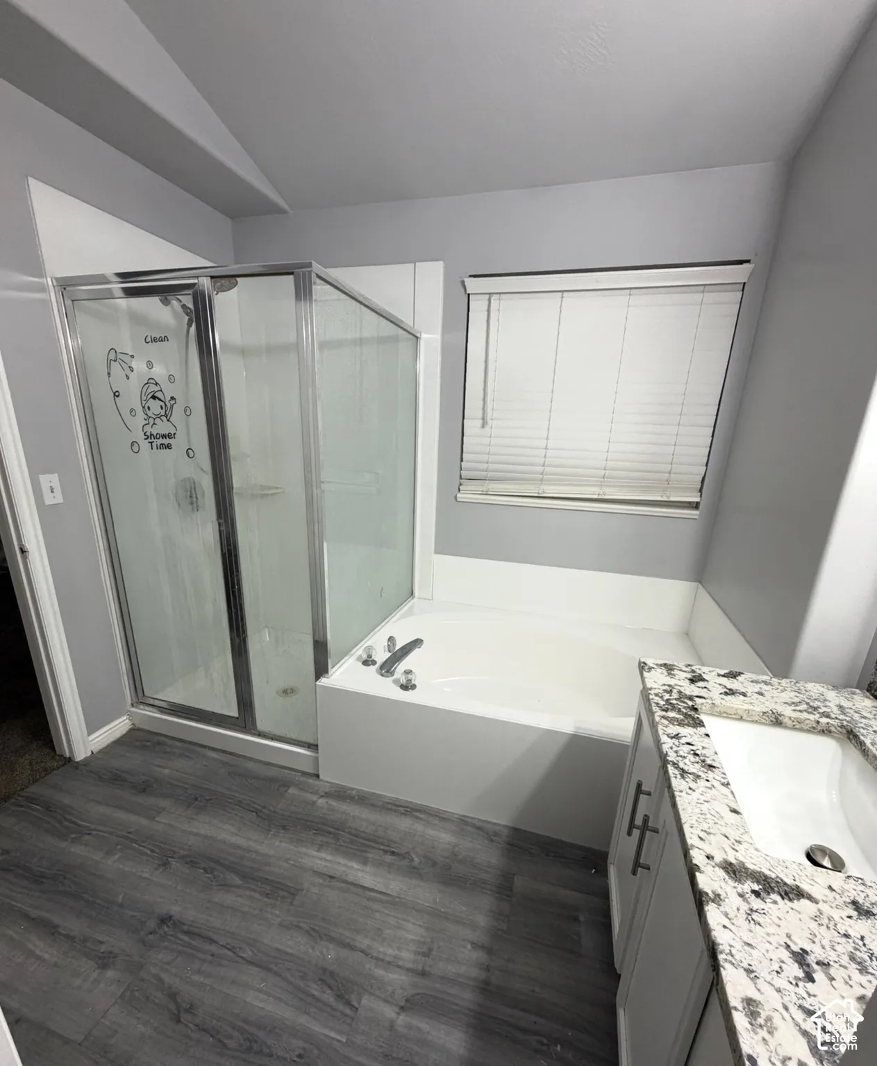 Bathroom featuring a shower stall with a glass enclosure, a deep soaking tub, stone-finish countertop, vanity cabinet with metal hardware, and wood-finish flooring