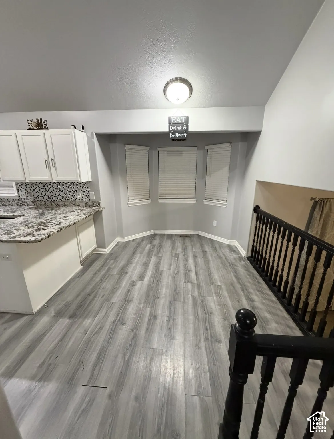 Vaulted ceilings, wood-finish flooring, bay window with blinds, stone-patterned countertops, and dark-finish balustrade railing