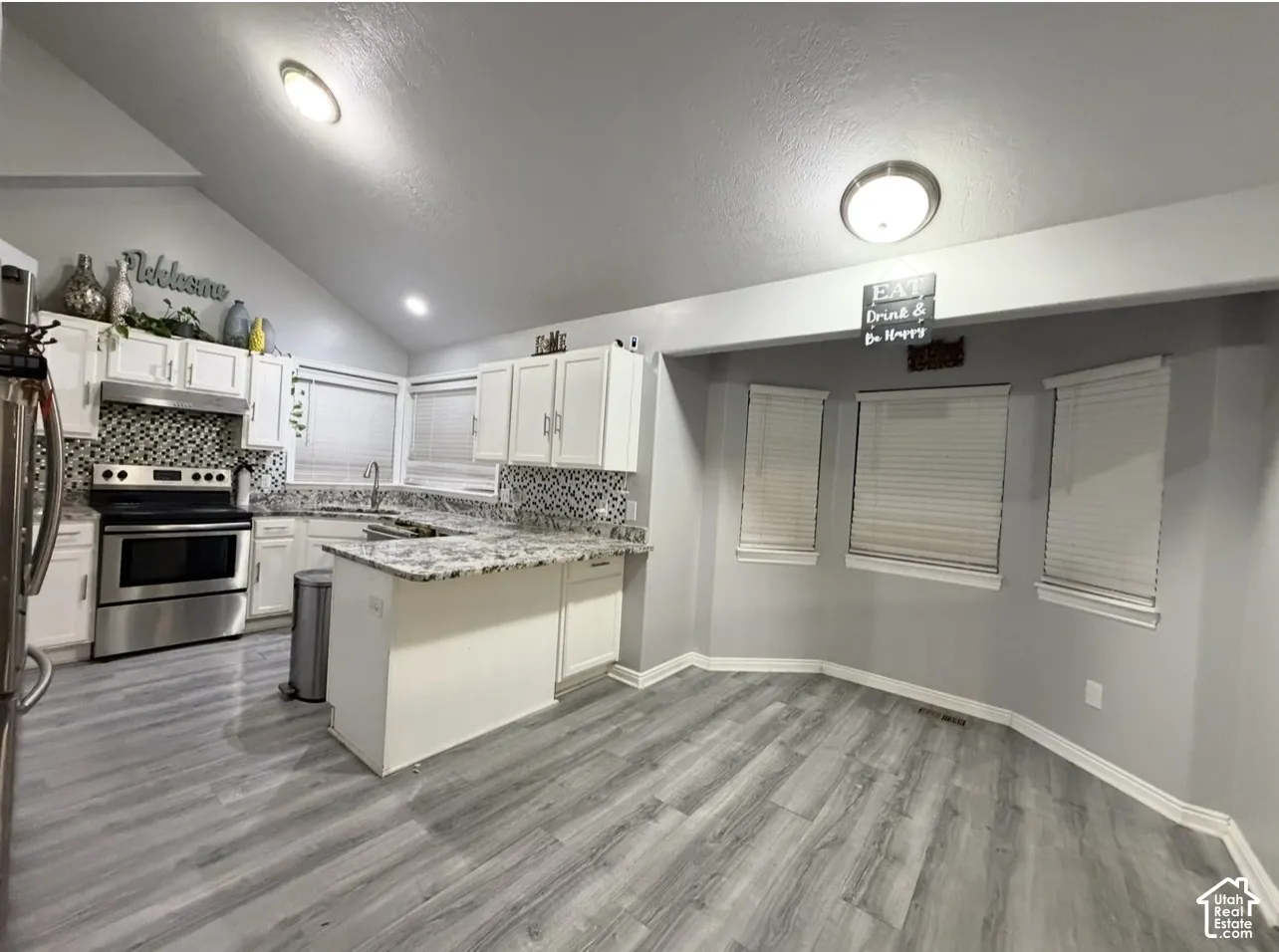 Kitchen featuring white cabinetry, stone-finish countertops, mosaic tile backsplash, wood-finish flooring, and a vaulted ceiling