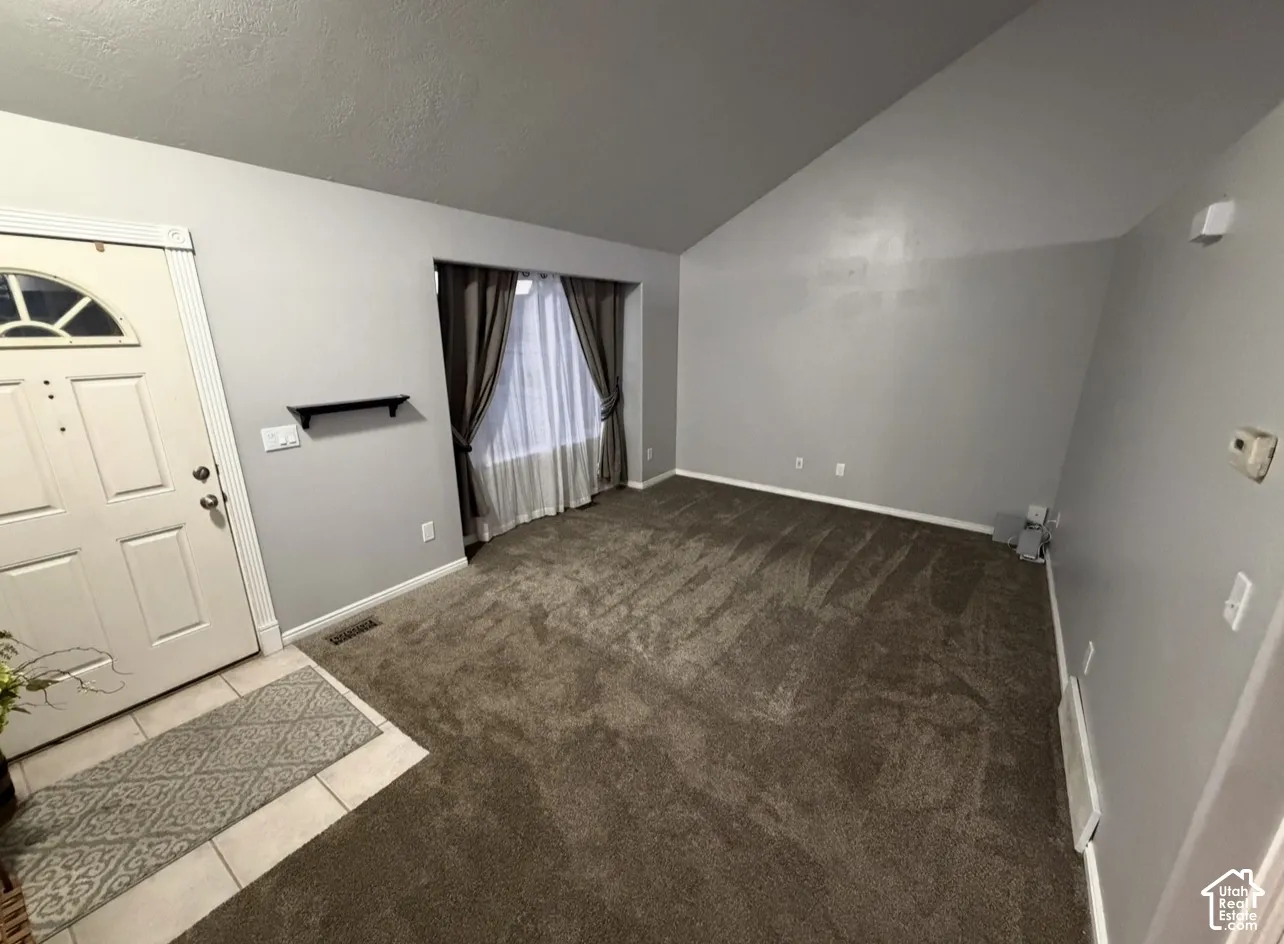 Vaulted ceiling, carpeted flooring, tile entryway, and natural lighting provided by a multi-pane window