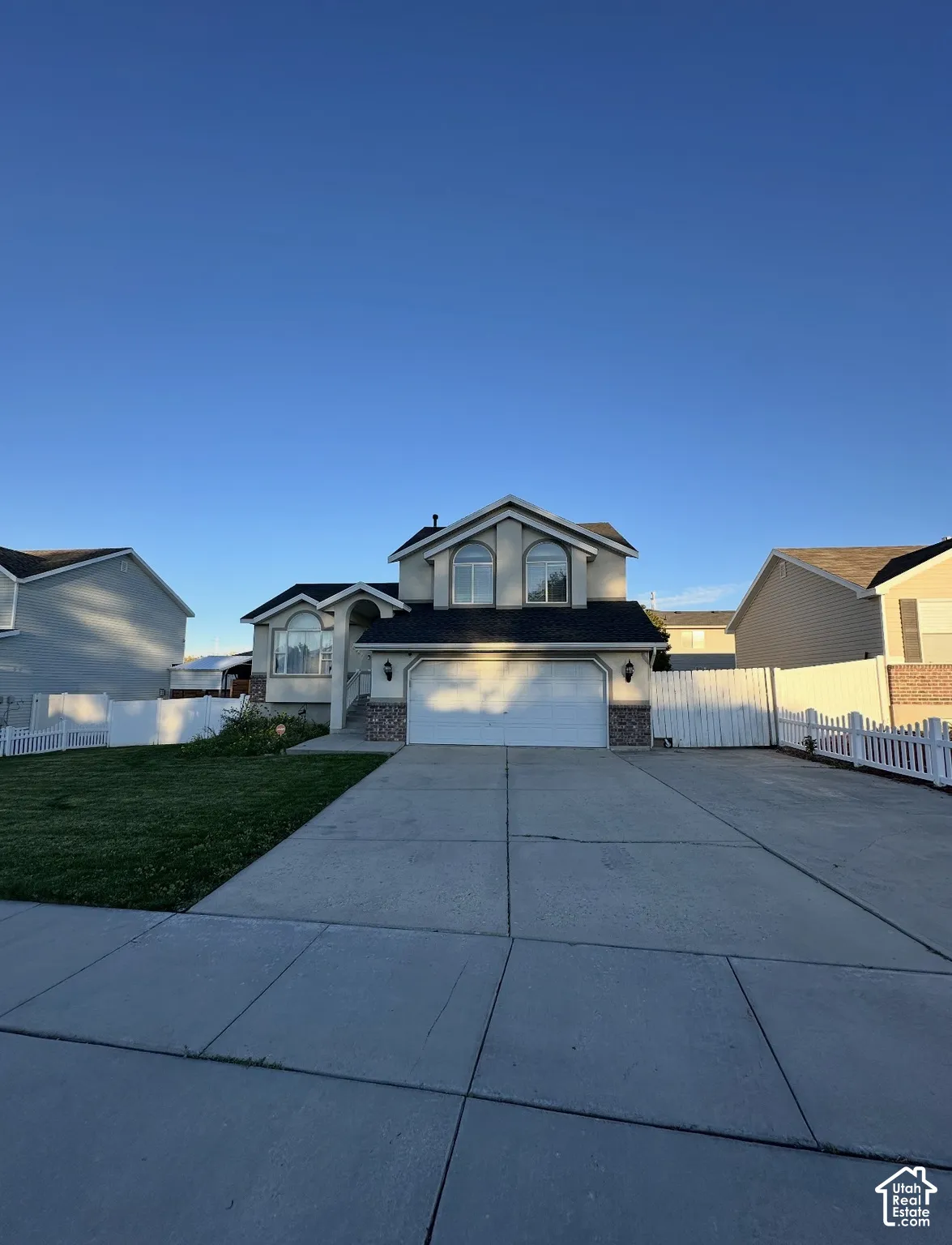 Multi-level exterior featuring a two-car garage, arched windows, concrete driveway, and white vinyl privacy fencing