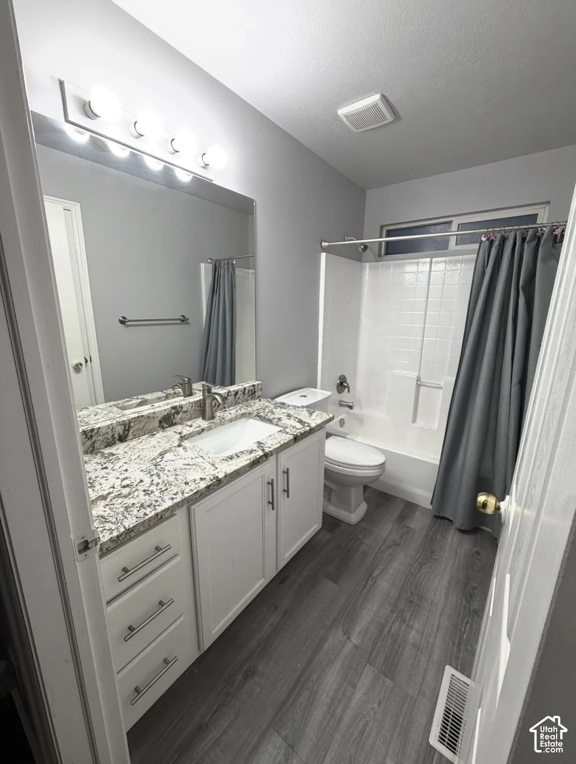 Bathroom featuring a white vanity cabinet, patterned stone-surface countertop with an integrated rectangular sink, wood-finish flooring, and a tub-shower combination with a surround