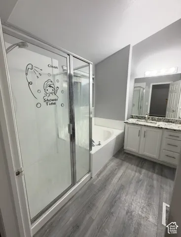Bathroom featuring wood-finish flooring, a white vanity with stone-pattern countertop, an integrated sink, a glass-enclosed shower, and a built-in soaking tub