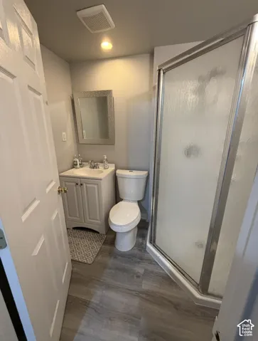 Bathroom featuring wood-finish flooring, a corner glass-enclosed shower, a white vanity with a composite countertop, and a wall-mounted rectangular mirror