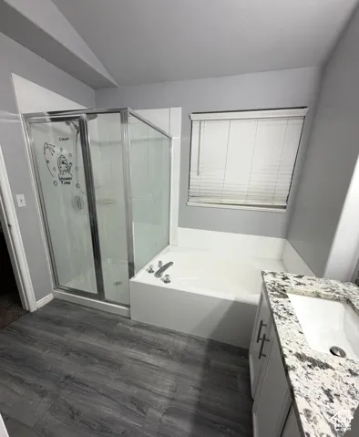 Bathroom featuring a shower stall with a glass enclosure, a deep soaking tub, stone-finish countertop, vanity cabinet with metal hardware, and wood-finish flooring
