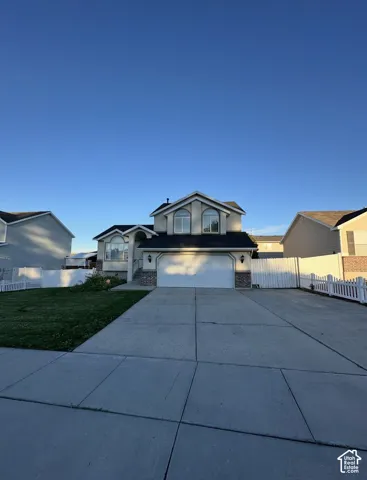 Multi-level exterior featuring a two-car garage, arched windows, concrete driveway, and white vinyl privacy fencing