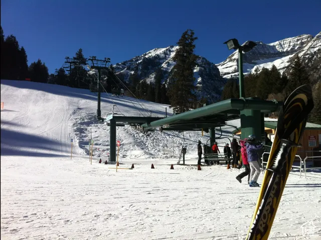 Mountain slope terrain featuring a mechanical chairlift, groomed snow coverage, and a backdrop of alpine peaks