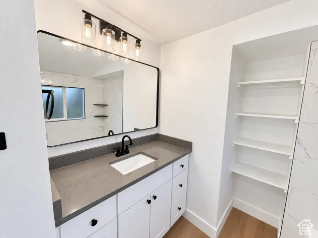 Bathroom vanity featuring a solid surface countertop, undermount sink, matte black hardware, integrated storage shelving, and framed wall mirror with a four-light fixture