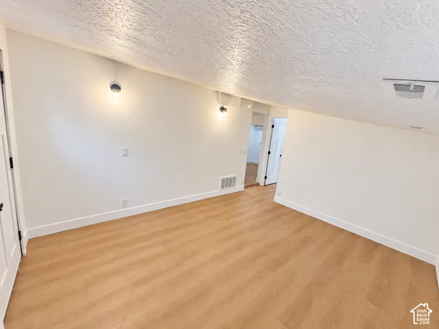 Room featuring sloped ceilings, wood-finish flooring, and wall-mounted light fixtures