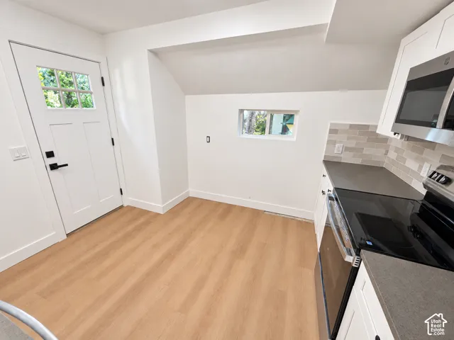 Kitchen featuring white cabinetry, wood-finish flooring, stone-composite countertops, subway tile backsplash, and stainless steel appliances