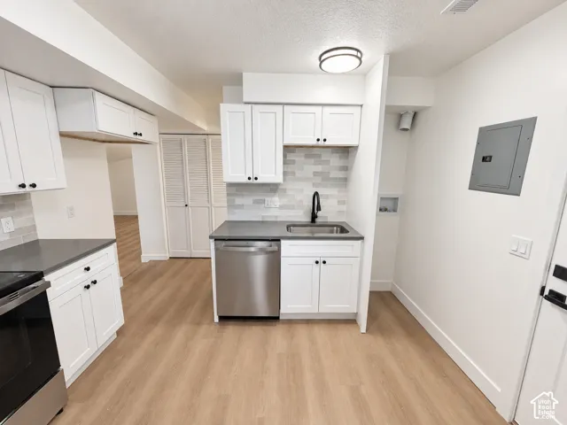 Kitchen featuring white shaker-style cabinetry, matte black hardware, stone-finish countertops, stainless steel dishwasher, and horizontal tile backsplash