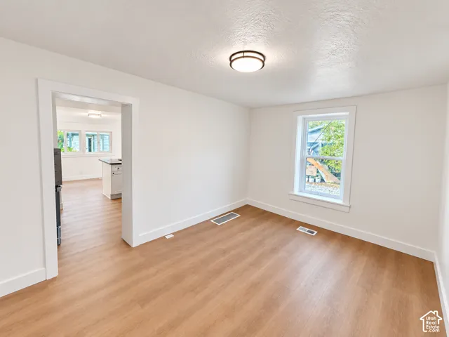 Room interior featuring light-toned wood-finish flooring, crisp white wall finishes, a dual-pane window with white trim, and a flush-mount circular ceiling fixture