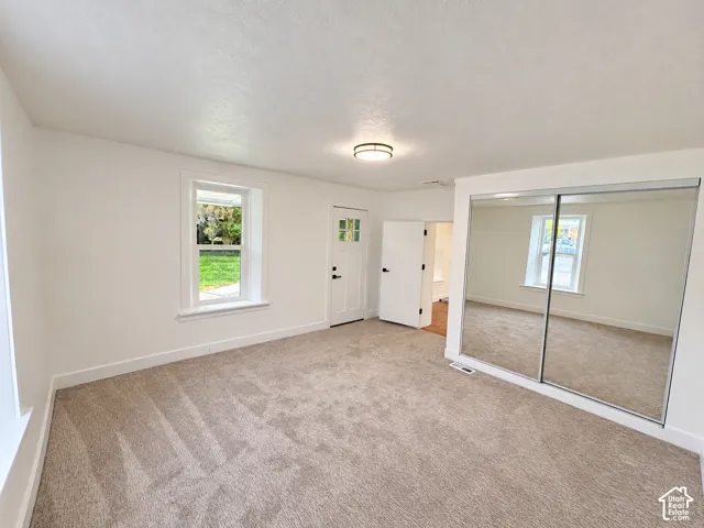 Neutral-toned carpeting, mirrored sliding closet doors, multi-pane window, and flush-mount ceiling lighting