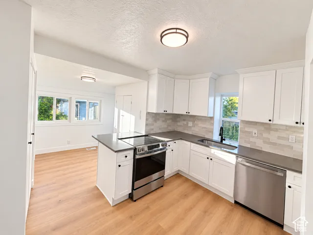 Kitchen featuring white cabinetry, quartz countertops, a brick-pattern tile backsplash, stainless steel appliances, and wood-finish flooring