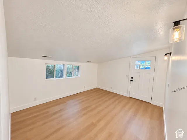 Interior space featuring a sloped ceiling, wood-finish flooring, dual windows with exterior exposure, and a single-lite paneled entry door with wall-mounted glass cylinder fixtures