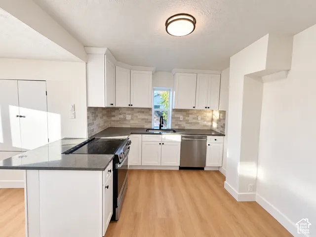Kitchen featuring white Shaker-style cabinetry, dark solid-surface countertops, a tiled backsplash, stainless steel appliances, and wood-finish flooring