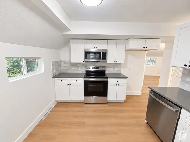 Kitchen featuring white cabinetry, stainless steel appliances, dark stone-finish countertops, and a light-toned subway tile backsplash with wood-finish flooring