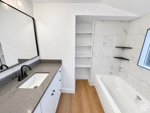 Bathroom featuring a vanity with a solid-surface countertop, rectangular undermount sink, matte black faucet, integrated white shelving, and a tub enclosure with stone-patterned wall tile and floating corner shelves