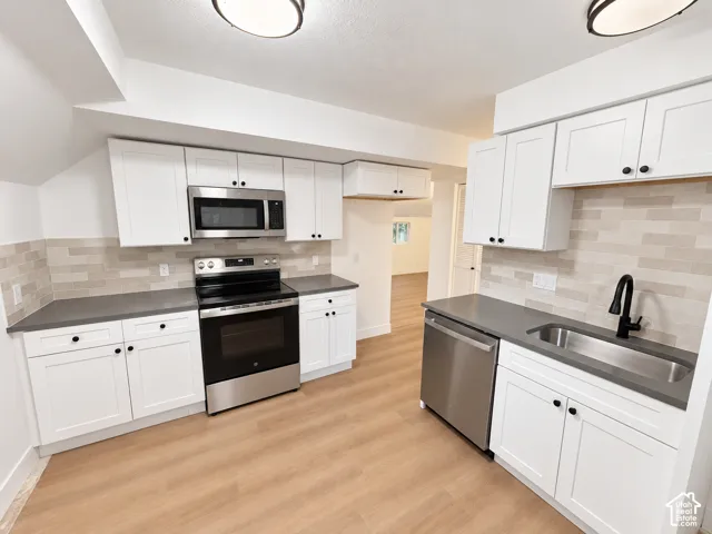 Kitchen featuring white shaker-style cabinetry, matte grey countertops, stainless steel appliances, a linear tile backsplash, and wood-finish flooring