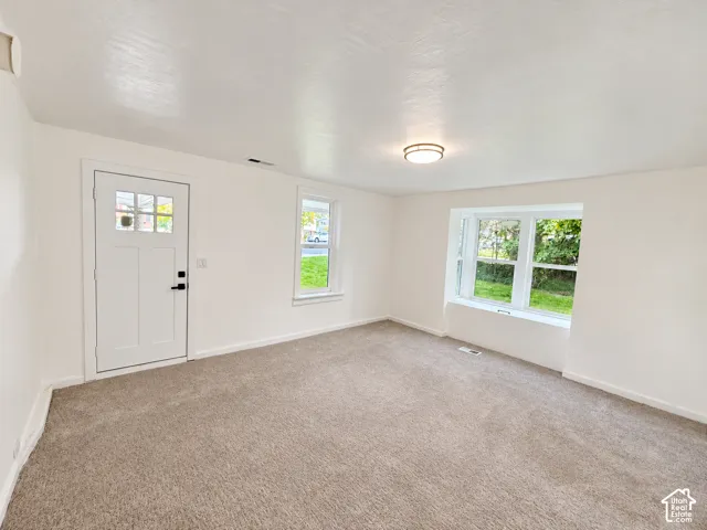 Neutral wall finishes, plush carpeting, a large bay window, and a single-light door featuring inset glass panes