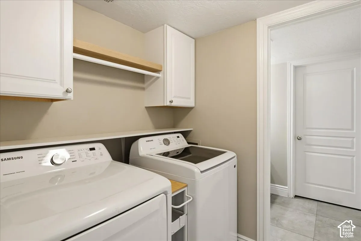 Laundry space featuring shaker-style upper cabinetry, natural wood-finish open shelving, and neutral tile flooring