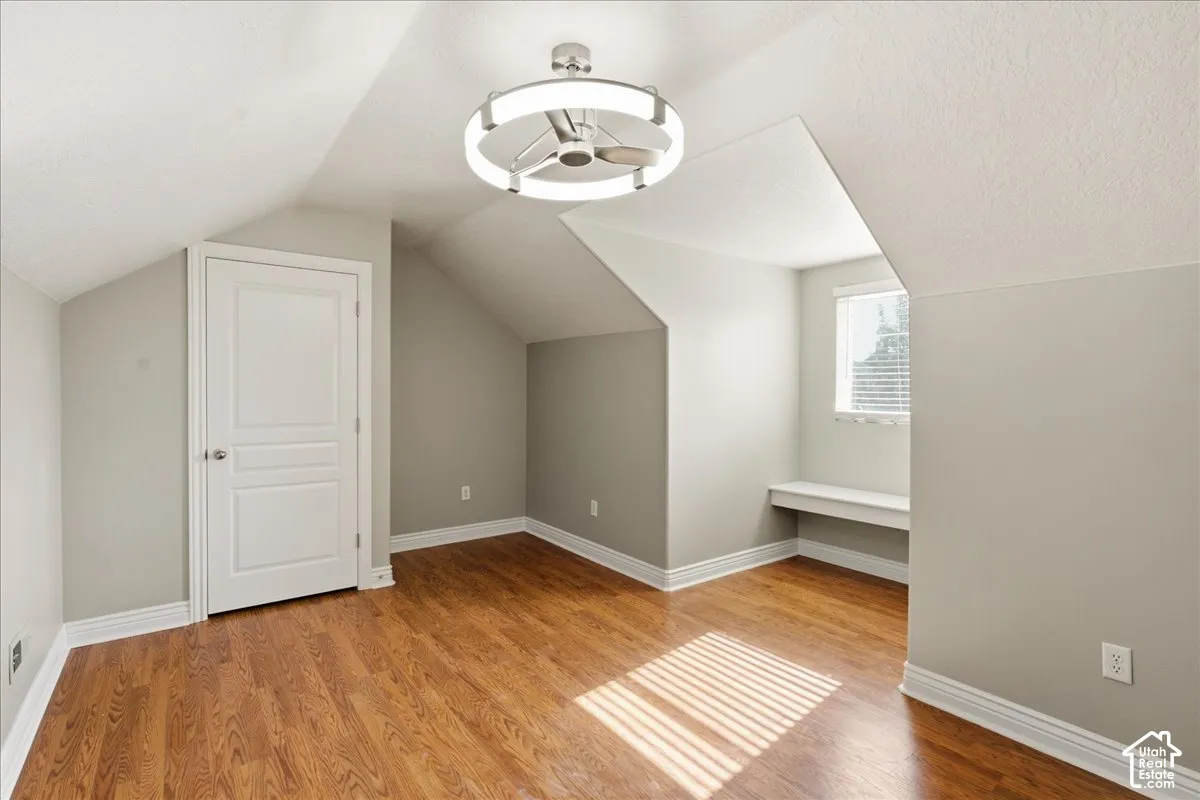 Interior space featuring wood-finish flooring, vaulted ceilings, a built-in window bench, and a modern circular LED light fixture
