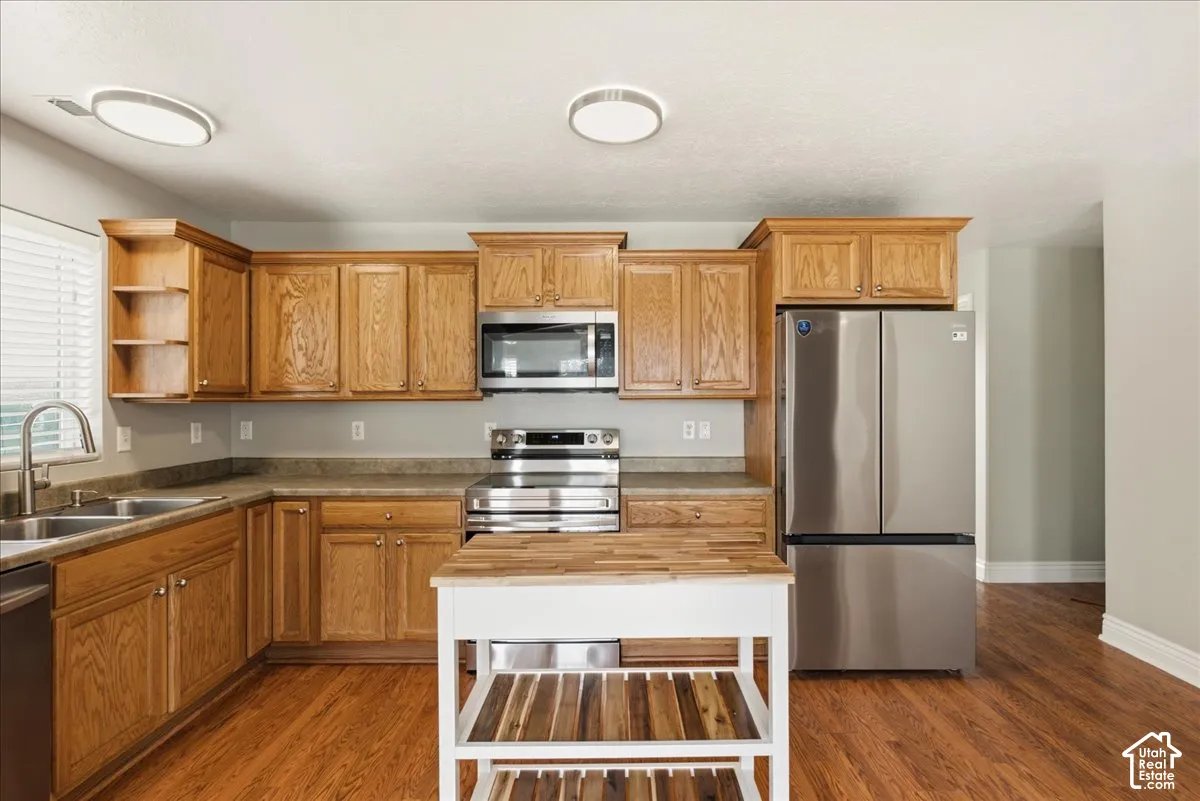Kitchen featuring natural wood cabinetry, stainless steel appliances, wood-finish flooring, and recessed ceiling lighting