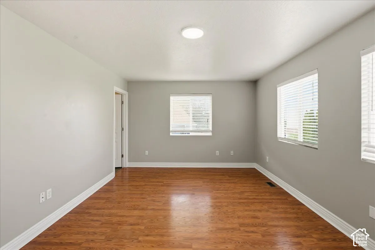 Neutral-toned walls, wood-finish flooring, and multiple windows with horizontal blinds