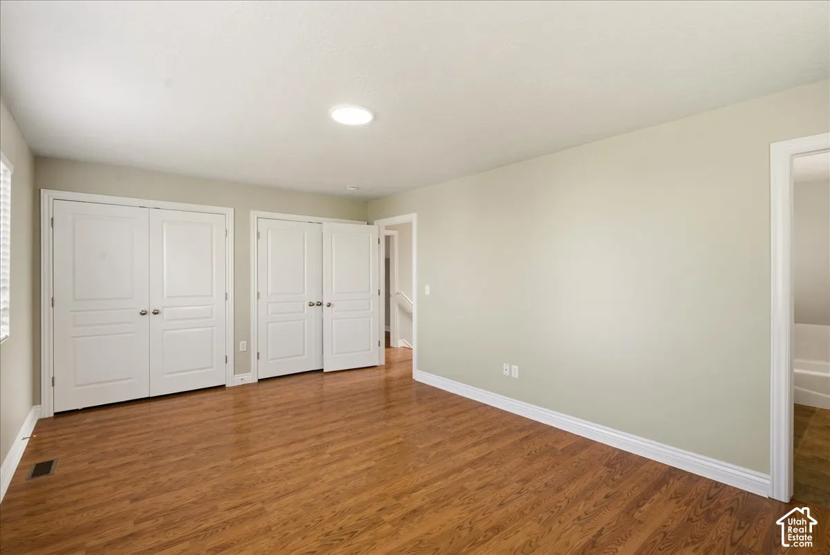 Room featuring wood-finish flooring, two sets of double-panel closet doors, and neutral wall paint